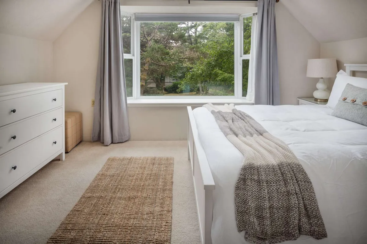 A serene bedroom filled with soft natural light, featuring a plush bed, elegant curtains, a simple dresser, and a cozy rug. The calming decor emphasizes tranquility and the promise of restful moments.