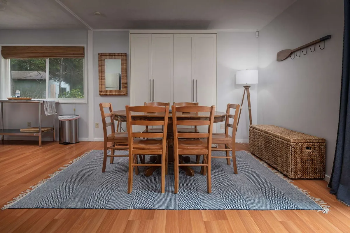 A cozy dining nook with a rustic table, woven rug, and soft lighting from a floor lamp. The space is set up for shared meals, social gatherings, or game nights, embodying comfort and togetherness.