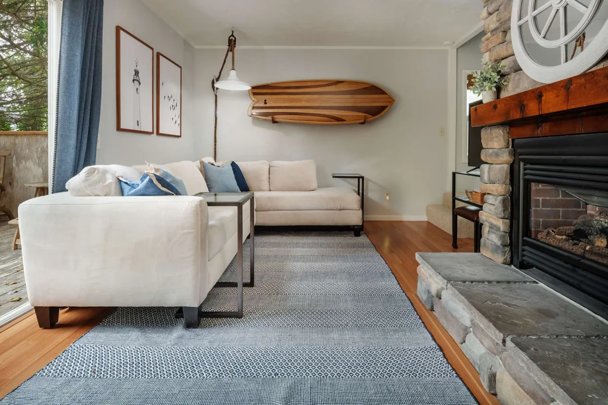 A cozy living room scene featuring a comfortable sofa facing a charming fireplace, with a wooden boat accent and tasteful artwork providing a sophisticated yet welcoming atmosphere. The firelight and soft furnishings invite relaxation and social connection.