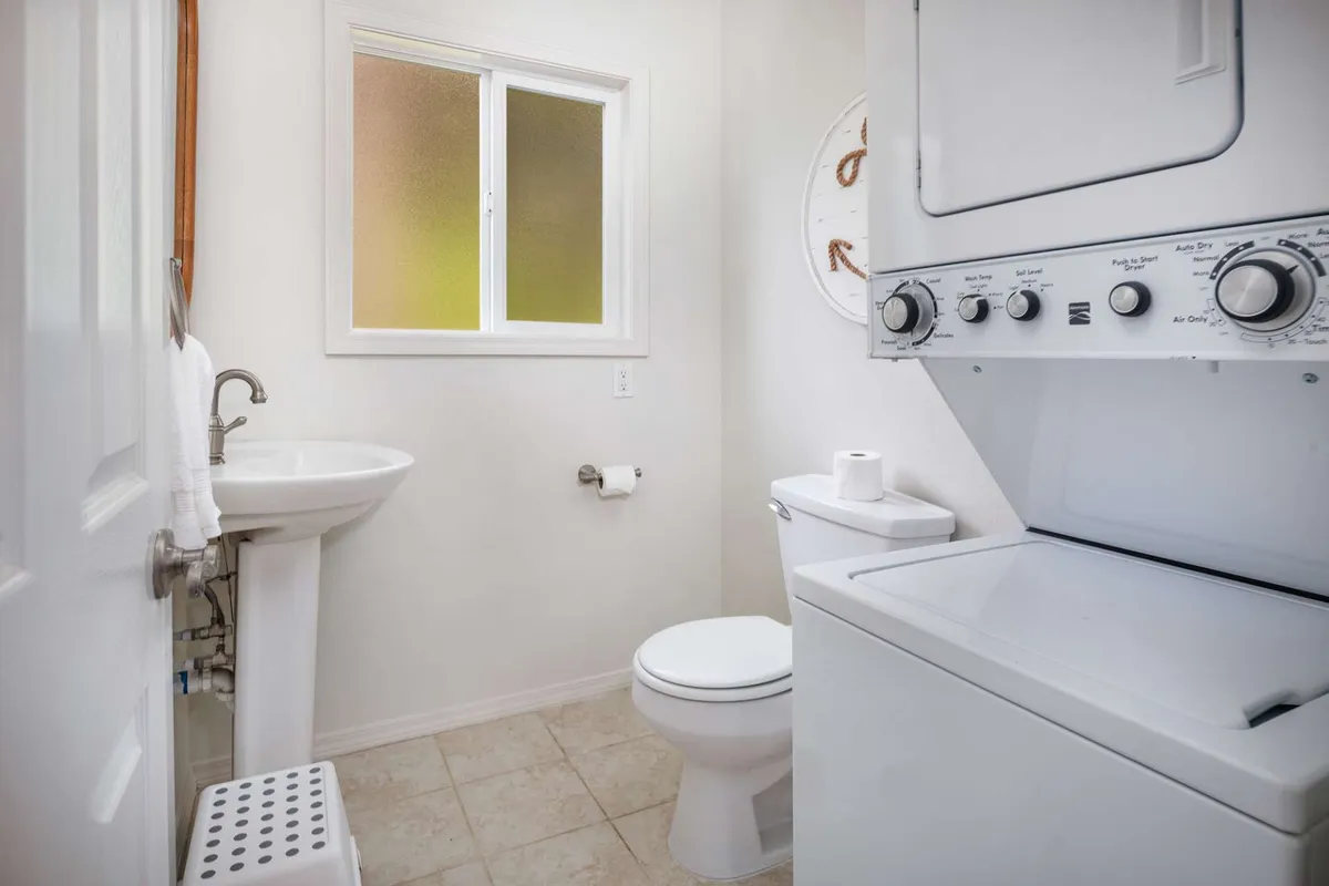 A practical main-floor half bath equipped with a modern washer and dryer, sink, and toilet. The space is neatly organized, with natural light from a window adding to its approachable feel. Ideal for families or guests needing accessible, convenient facilities.