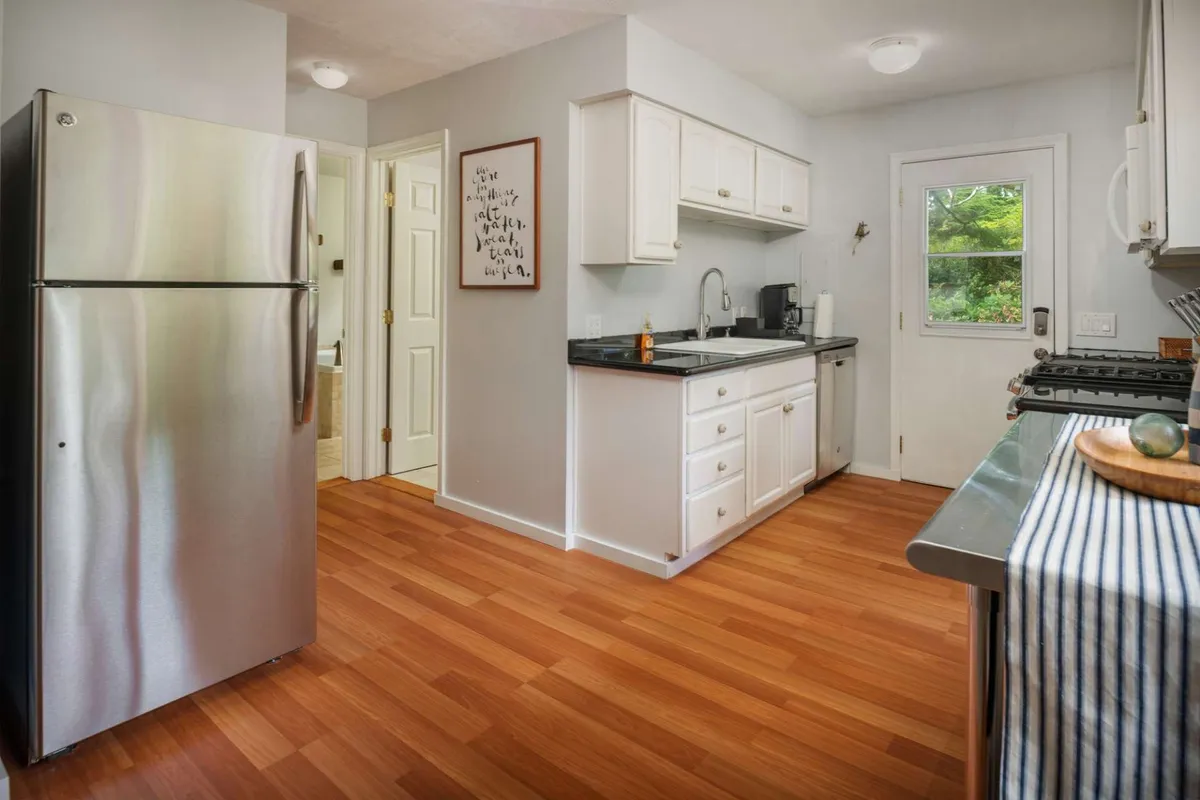 A bright, welcoming kitchen scene with white cabinets, a stainless steel refrigerator, black countertop, and, most importantly, durable wooden flooring that’s easy to clean. The open layout suggests a practical space ideal for pet owners, making daily routines with pets stress-free.